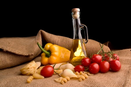 Image of olive oil, tomatoes, peppers, garlic and pasta on burlap cloth with black background