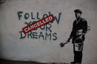 Graffiti on a wall reading "Follow Your Dreams" with a red "Cancelled" sticker on top
