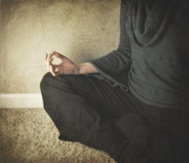 Person sitting in lotus position on carpet and meditating